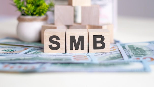 Le mot SMB est écrit sur des cubes en bois. les cubes sont situés sur les billets posés sur la table. en arrière-plan une plante verte dans un pot. SMB - abréviation de Server Message Block