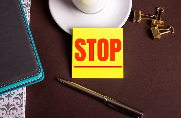 Le mot STOP écrit sur papier jaune sur fond marron près d'une tasse de café et de journaux