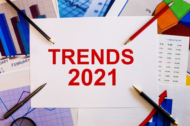 Le mot TRENDS 2021 est écrit sur un fond blanc à proximité de graphiques colorés, de stylos et de crayons. Concept d'entreprise