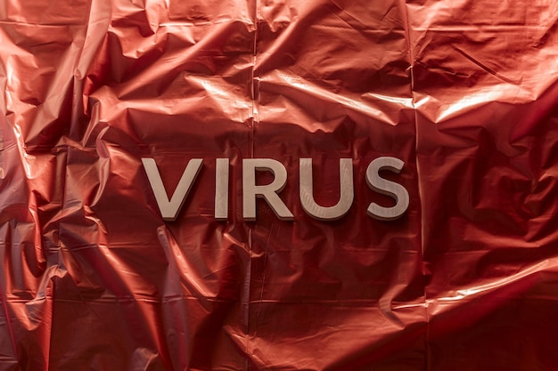 Le mot virus posé avec des lettres en métal argenté sur fond rouge de film plastique froissé avec une lumière dramatique
