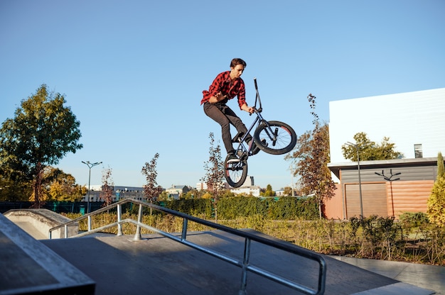 Motard bmx mâle, sauter en action, adolescent en formation dans le skatepark. Sport de vélo extrême, exercice de cyclisme dangereux, conduite de rue à risque, vélo dans le parc d'été