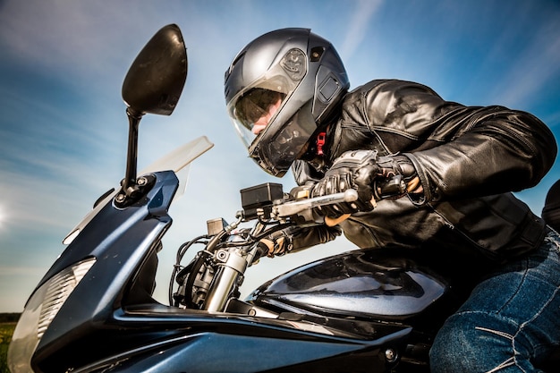 Motard en casque et veste en cuir course sur route