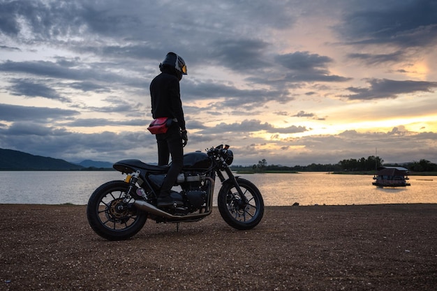 Un motard debout sur un grand vélo vintage avec un ciel coloré au réservoir