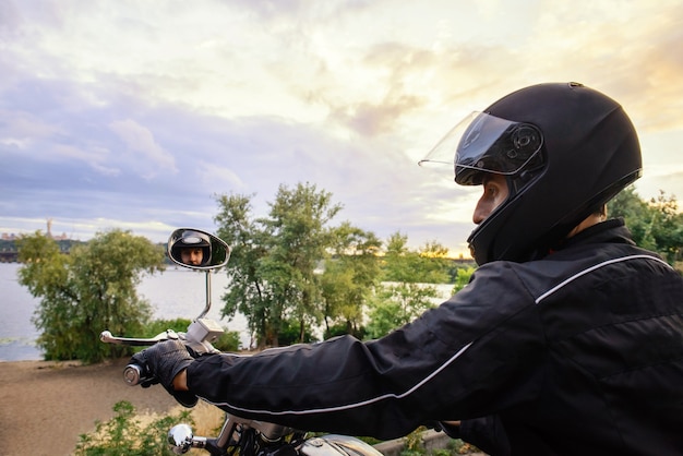 Motard en moto de conduite de casque au coucher du soleil. Route près de la rivière dans la ville. Concept de transport sûr.