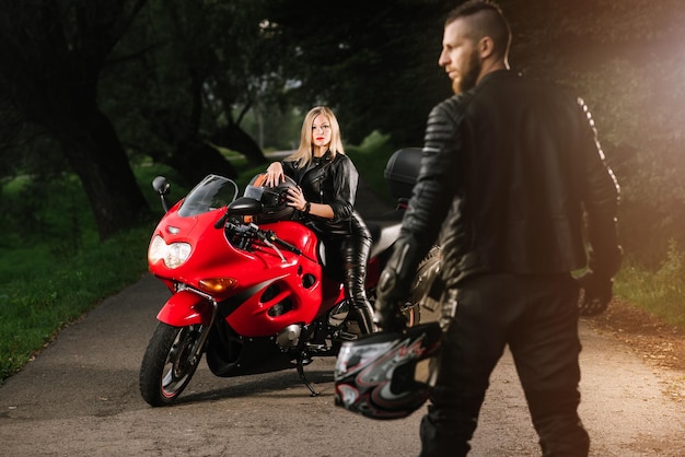 Motards homme et femme en vestes de cuir avec moto de sport sur la route le soir