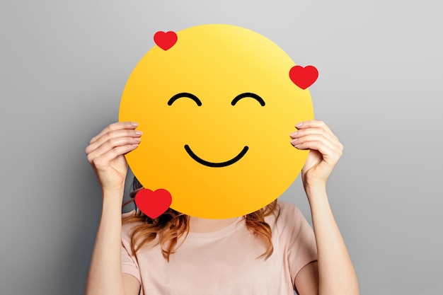 Émoticône amoureuse La fille tient un smiley jaune avec une émoticône de visage d'amour romantique