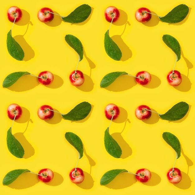 Motif créatif régulier sans couture à partir de petites pommes rouges mûres et de feuilles vertes sur fond jaune