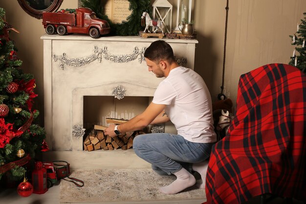 Photo motif de noël un jeune homme met du bois de chauffage dans la cheminée