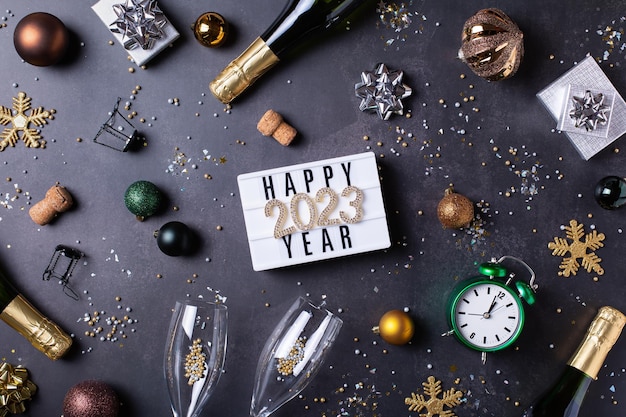 Photo motif de la nouvelle année avec des verres de champagne, des bouteilles, des confettis étincelants et le nombre de 2023 à plat