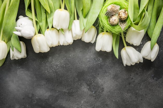 Motif de Pâques. Bordure de tulipes blanches, œufs, nid sur gris vintage. Vue de dessus avec espace copie.