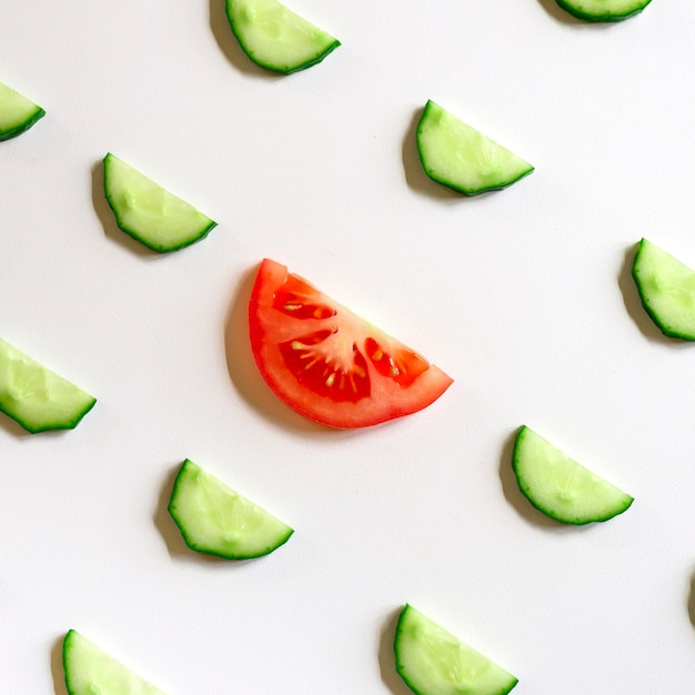 Motif répétitif de demi-cercles tranchés de concombres de légumes crus frais pour salade et une tranche de tomate au centre isolé sur fond blanc à plat, vue de dessus. carré