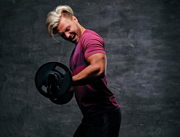 Émotionnel, hurlant, athlétique, homme blond faisant un entraînement de biceps avec une barre.