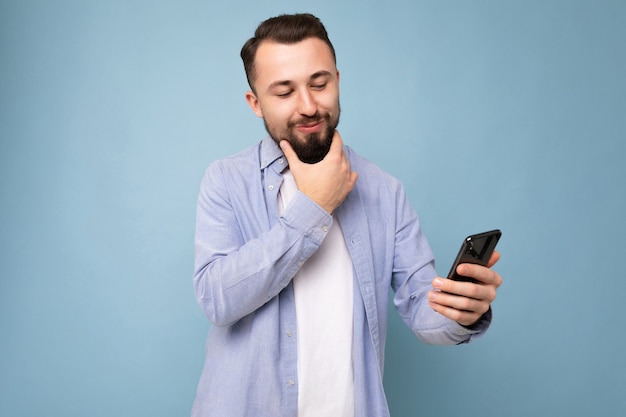 Émotionnel positif beau jeune homme barbu brunet vêtu d'une chemise bleue décontractée et d'un t-shirt blanc