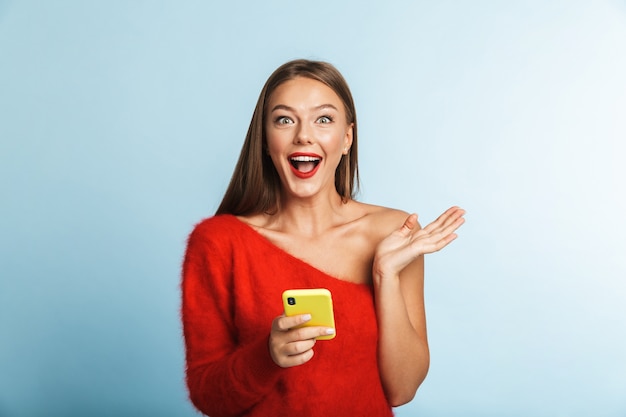 Émotionnelle excitée jeune femme posant isolée, à l'aide de téléphone mobile.