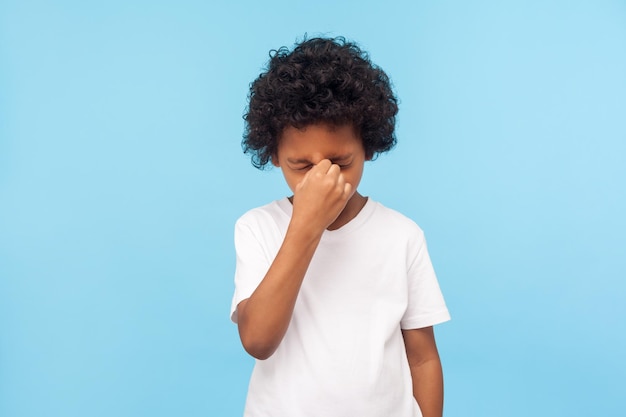 Émotions dramatiques d'un enfant malheureux Profil d'un petit garçon triste aux cheveux bouclés grimaçant et pleurant en se frottant les yeux pour essuyer les larmes prise de vue en studio à l'intérieur isolée sur fond bleu espace de copie pour l'annonce