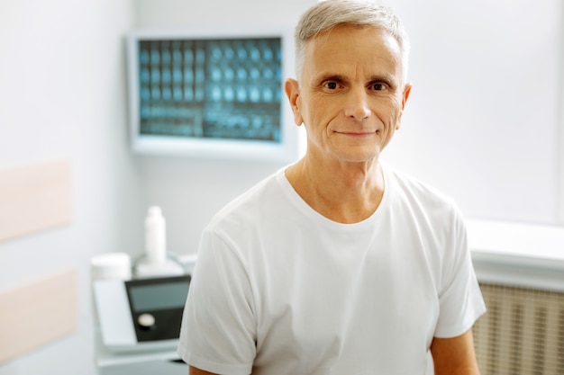 Émotions positives. Heureux bel homme âgé assis dans le bureau du médecin et vous souriant tout en étant de bonne humeur