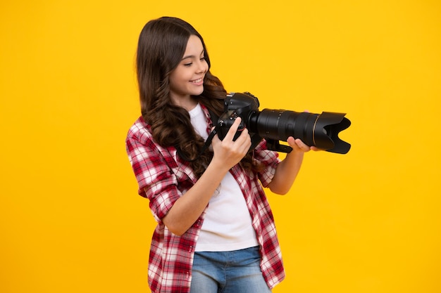 Émotions positives et souriantes d'une adolescente avec un appareil photo professionnel dslr avec un grand objectif photo Photographe enfant isoalted sur fond jaune Photo school