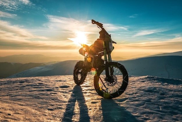 Une moto avec des chaînes sur roues se dresse au sommet d'une montagne en hiver