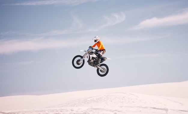 Moto ciel et sauter avec un homme dans le désert à cheval sur un véhicule pour l'aventure ou l'adrénaline vitesse de vélo et l'entraînement sur le sable avec un athlète dans l'air dans la nature pour la liberté ou la compétition active