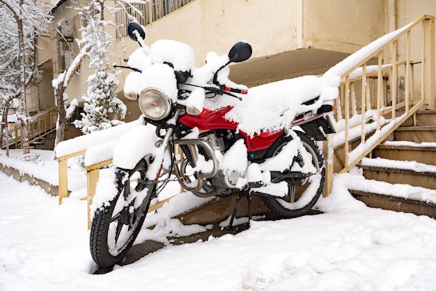 Moto couverte de neige dans la cour de la maison en hiver