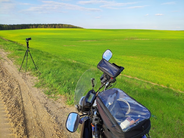 Une moto est garée sur un chemin de terre avec un champ vert en arrière-plan.