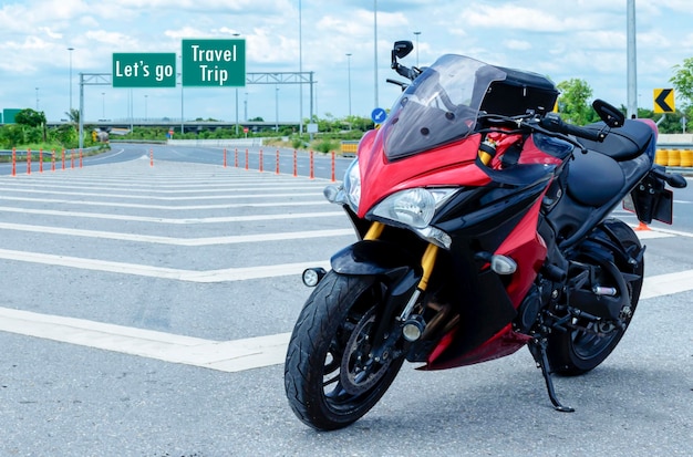 Moto rouge garée sur route avec message Let's go Travel Trip sur fond de signalisation verte