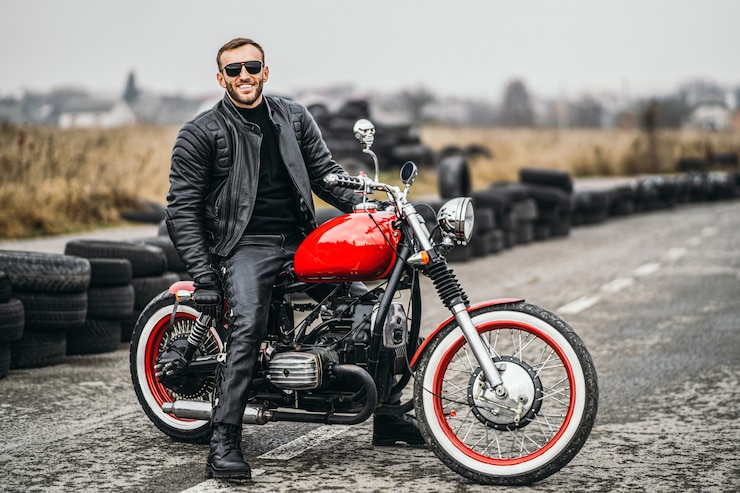 Photo moto rouge avec pilote. homme dans une veste et un pantalon en cuir noir se tient sur le côté au milieu de la route.