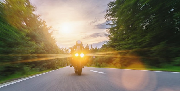 moto sur la route forestière à cheval. conduire sur la route vide lors d'un tour en moto au coucher du soleil. copyspace pour votre texte individuel.