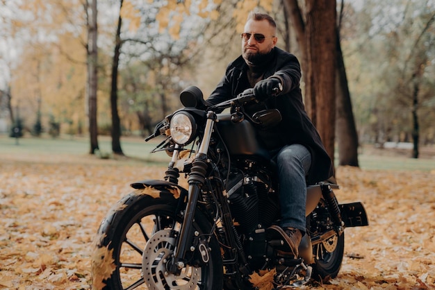 Un motocycliste masculin conduit dans la nature sur un vélo rapide porte des lunettes de soleil noires, des gants, des jeans et des bottes aime la saison d'automne passe du temps libre activement prêt pour un long voyage Conduite de transport de personnes