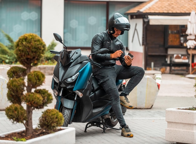 Un motocycliste moderne s'appuyant sur une moto mange sucré pendant une pause du travail