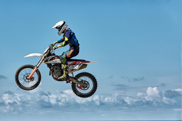 Le motocycliste de saut de moto de sport extrême fait un saut extrême contre le ciel.