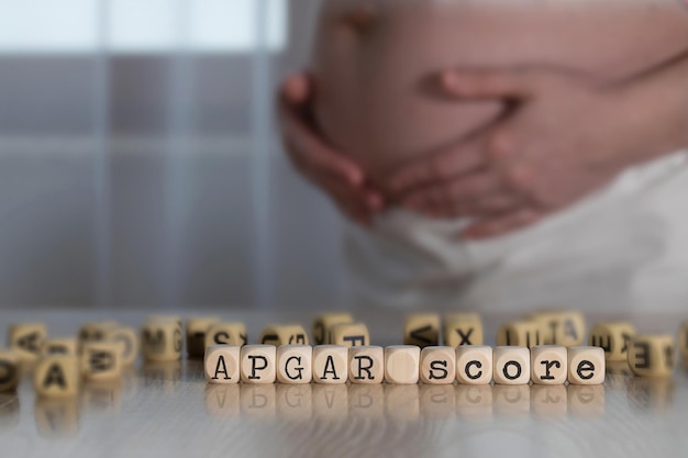 Mots APGAR SCORE composés de lettres en bois. Femme enceinte en arrière-plan