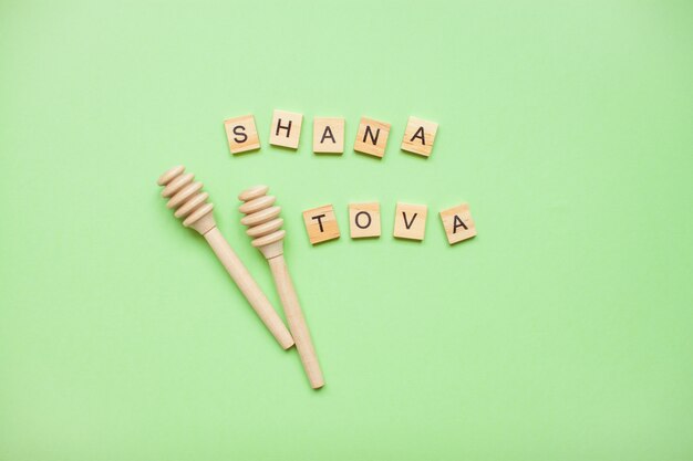 Mots de blocs de bois "shana tova" et cuillères en bois pour le miel sur un vert.