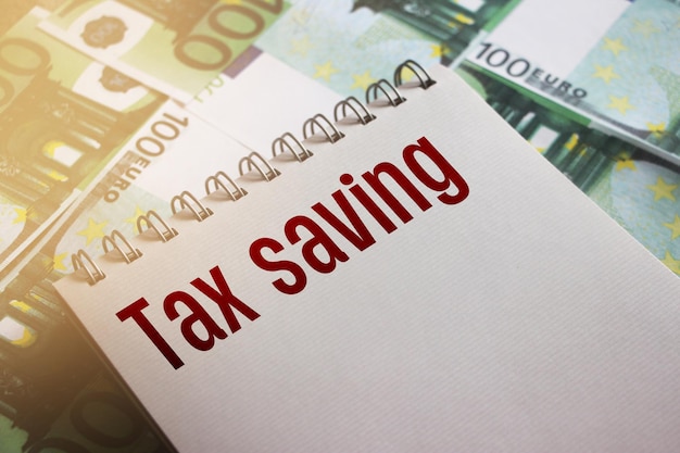 Mots d'économie d'impôt sur la page de cahiers portant sur des factures de 100 euros Frais et taxes concept financier