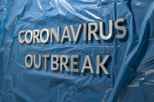 Les mots épidémie de coronavirus posés avec des lettres en métal argenté sur un film plastique bleu froissé