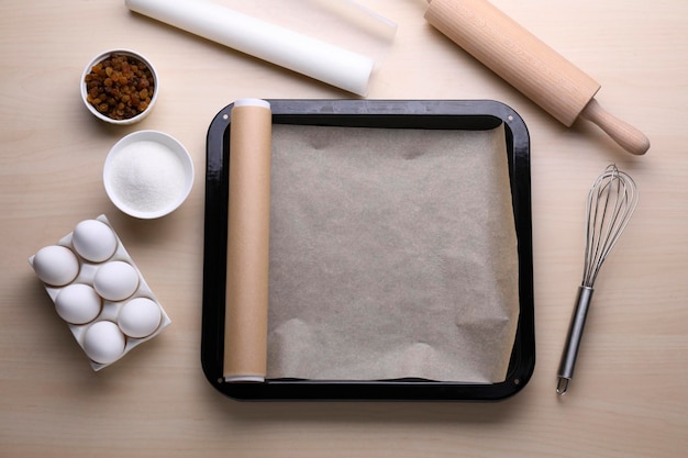 Moule à pâtisserie avec du papier sulfurisé différents ingrédients et ustensiles de cuisine sur une table en bois à plat