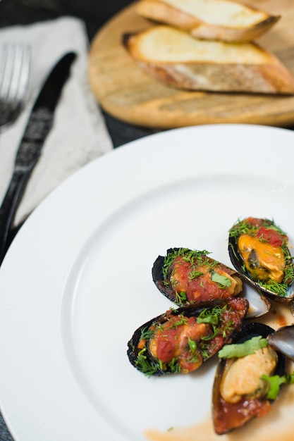 Moules au four à la sauce tomate avec coriandre et parmesan sur une assiette blanche.