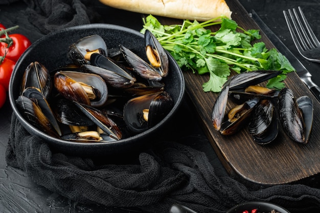 Moules bouillies dans des coquilles avec des épices et des herbes, dans un bol, sur fond noir