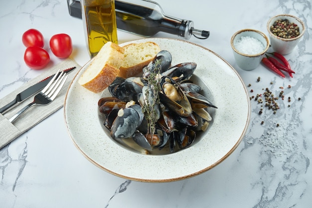 Moules chiliennes bouillies appétissantes dans une sauce crémeuse à l'ail avec croûtons dans une assiette blanche sur une surface en marbre