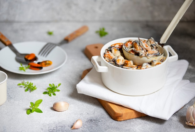 Moules à la crème et sauce au vin blanc. Servi avec de l'ail et des herbes dans une poêle blanche avec une louche. Plat gastronomique de fruits de mer. Fond gris clair. Vue de face