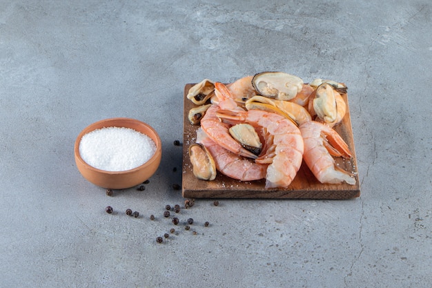 Moules et crevettes sur une planche à côté du sel, sur la surface en marbre.