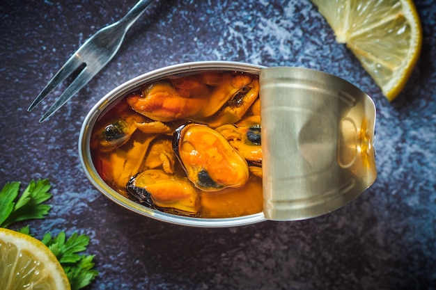 Photo moules marinées en conserve ouvertes sur une table bleu foncé avec citron et persil