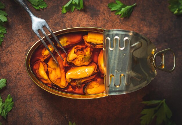 Photo moules marinées en conserve ouvertes sur une table marron foncé avec une fourchette et du persil