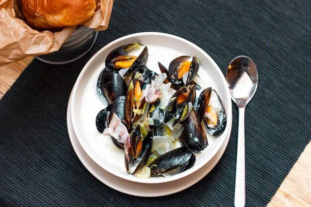 Photo des moules avec des oignons et du bacon dans de la sauce à la crème dans une assiette profonde avec du pain sur la table