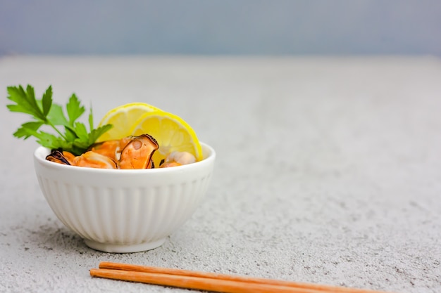 Moules sans coquille avec des tranches de citron dans un bol en céramique blanche.