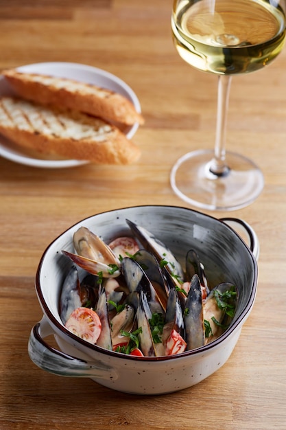 Photo moules avec sauce et pain grillé dans une assiette sur une table en bois avec un verre de vin blanc à proximité et un fond sombre. concept de restauration