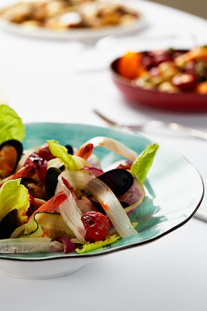 Moules vongoli dans une assiette avec laitue, moules cuites dans une sauce au vin blanc, fruits de mer servis par le chef, sur fond clair, gros plan.