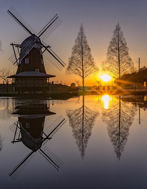 Moulin à vent traditionnel au bord d'un lac contre le ciel au coucher du soleil