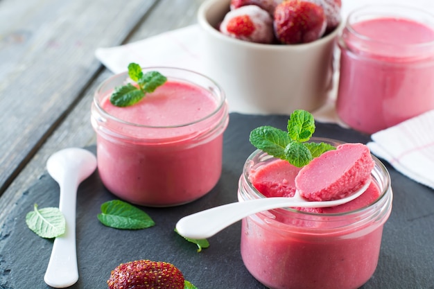 Mousse aux fraises dans des bocaux en verre et fraises congelées sur un vieux fond de table en bois.