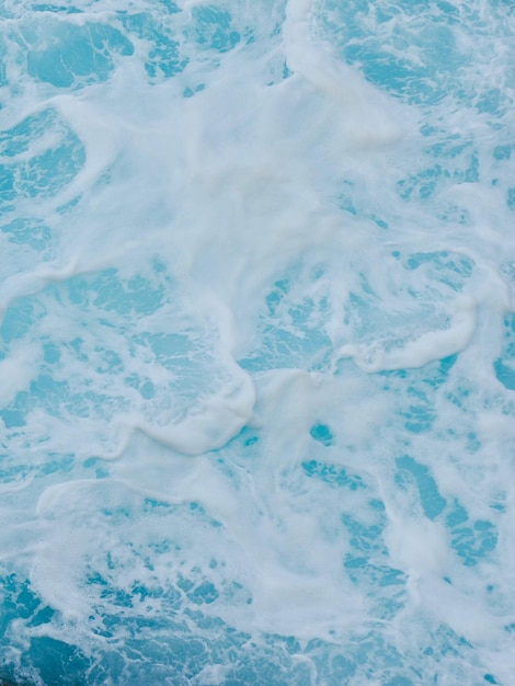 Mousse de mer blanche sur la surface de l'eau bleu clair Fond de nature colorée vive